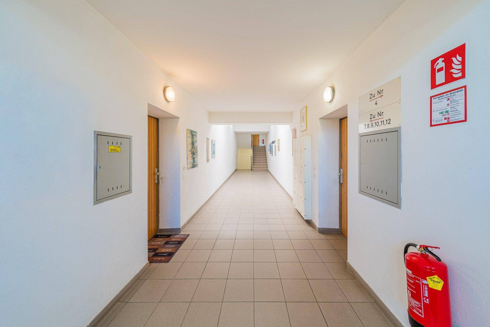 Langer Flur im Mehrfamilienhaus mit Fliesenboden und Zugang zu den Wohneinheiten.