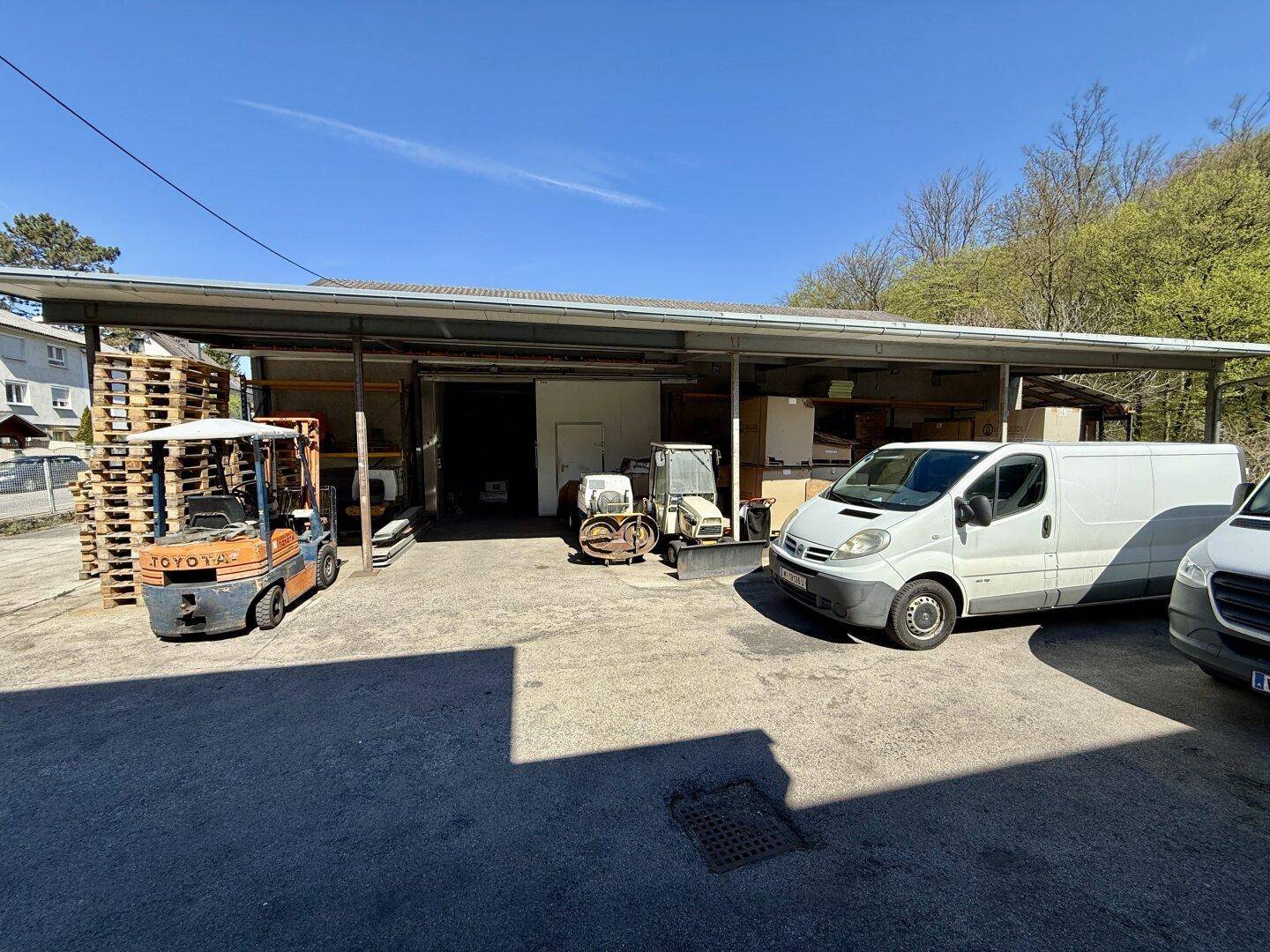 Außenansicht eines Gewerbegebäudes mit überdachtem Bereich, Lieferwagen und Gabelstapler auf dem Vorplatz.