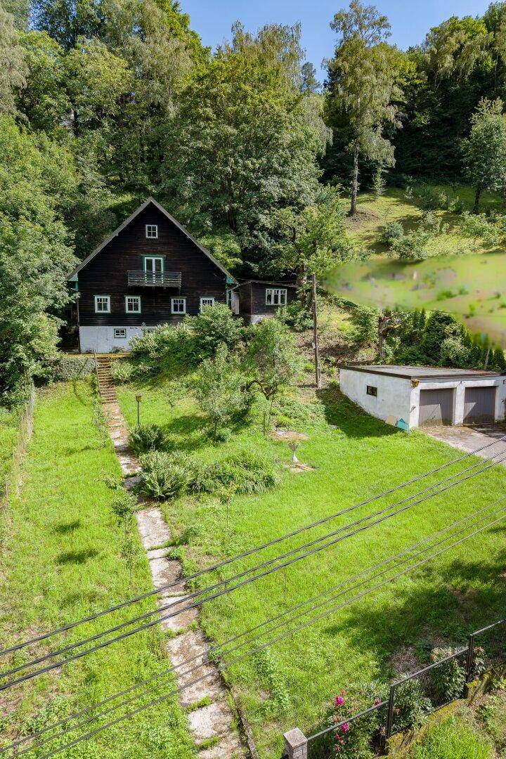 Das dunkle Holzhaus mit weißem Sockel und Doppelgarage, eingebettet in eine grüne Gartenlandschaft.