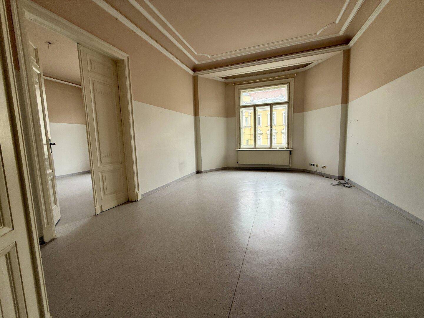 Büroraum mit Terrazzoboden und Stuckdecke, der durch ein großes Fenster viel Licht erhält.