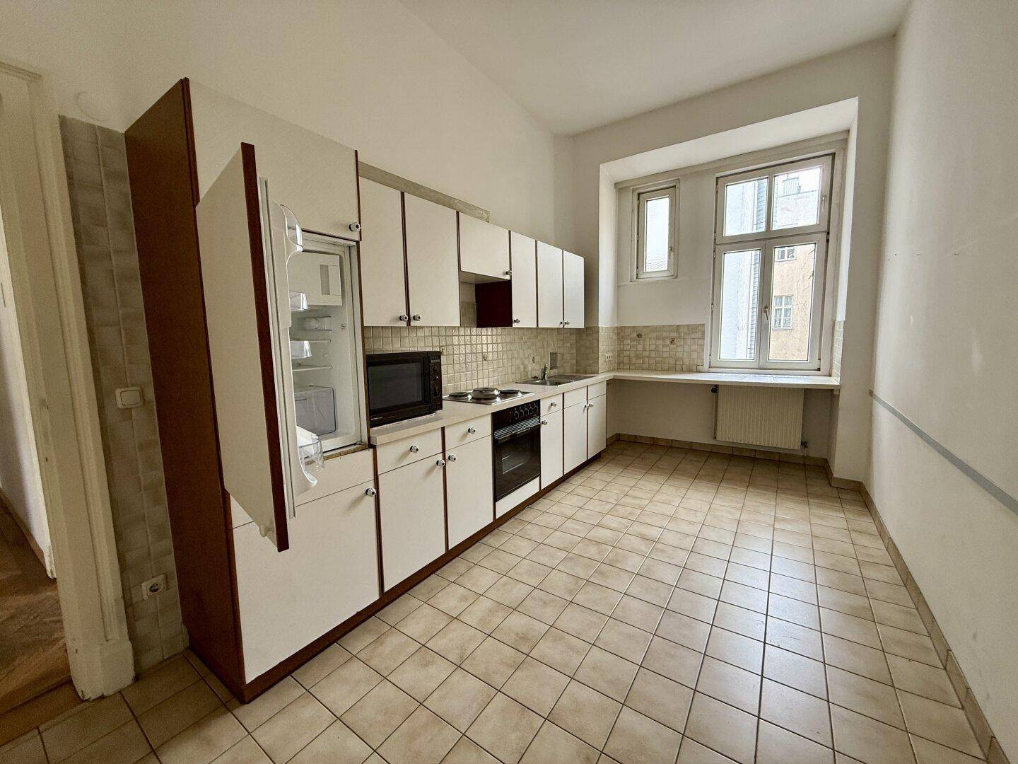 Funktionale Küche mit weißen Schränken, Fliesenboden und Fenster, bereit zur Nutzung.