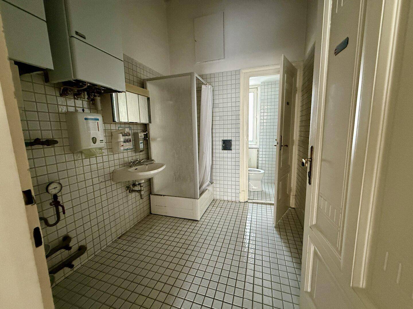Badezimmer mit Duschkabine, Waschbecken und Fliesenboden, in einem funktionalen Zustand.