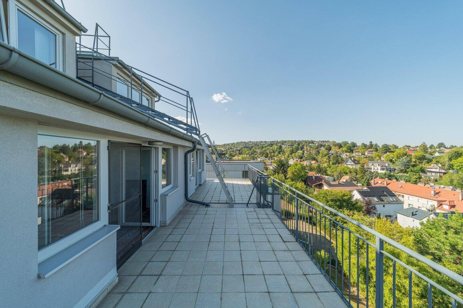 Weitläufige Terrasse mit Fliesenboden und Panoramablick auf die grüne Umgebung und die Dächer der Stadt.