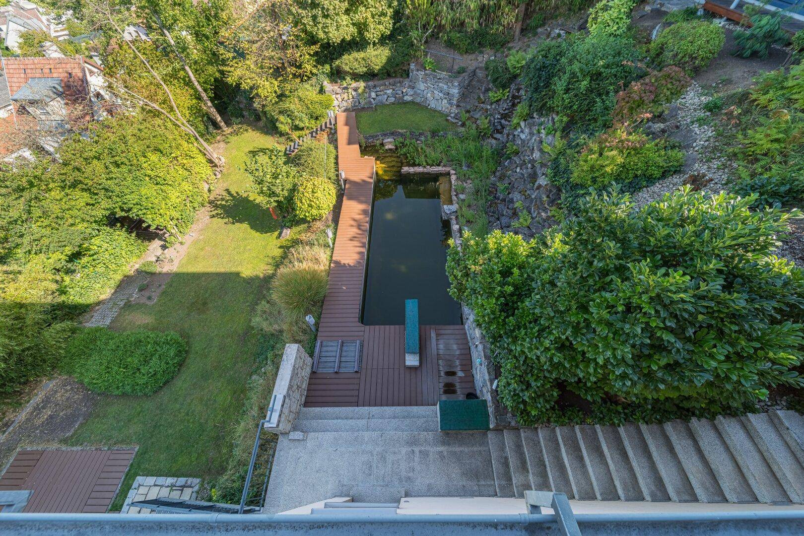 Vogelperspektive auf den terrassierten Gartenbereich mit langem Wasserbecken, Holzsteg und Steintreppen.