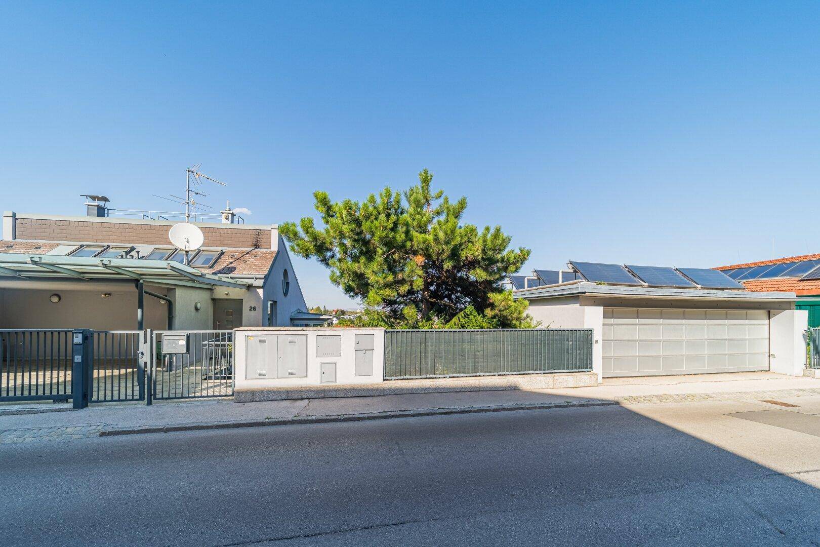 Straßenansicht eines modernen Gebäudes mit Garage, Carport und Photovoltaikanlage auf dem Dach.