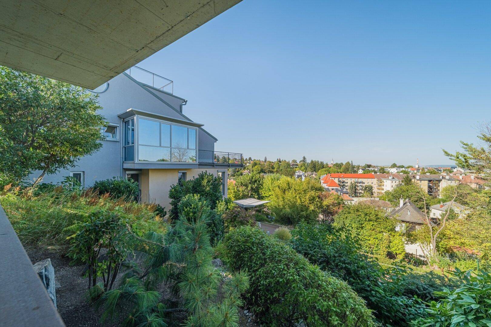 Panoramablick von einem Balkon auf die moderne Gebäudefassade mit großen Fenstern und die grüne Umgebung.