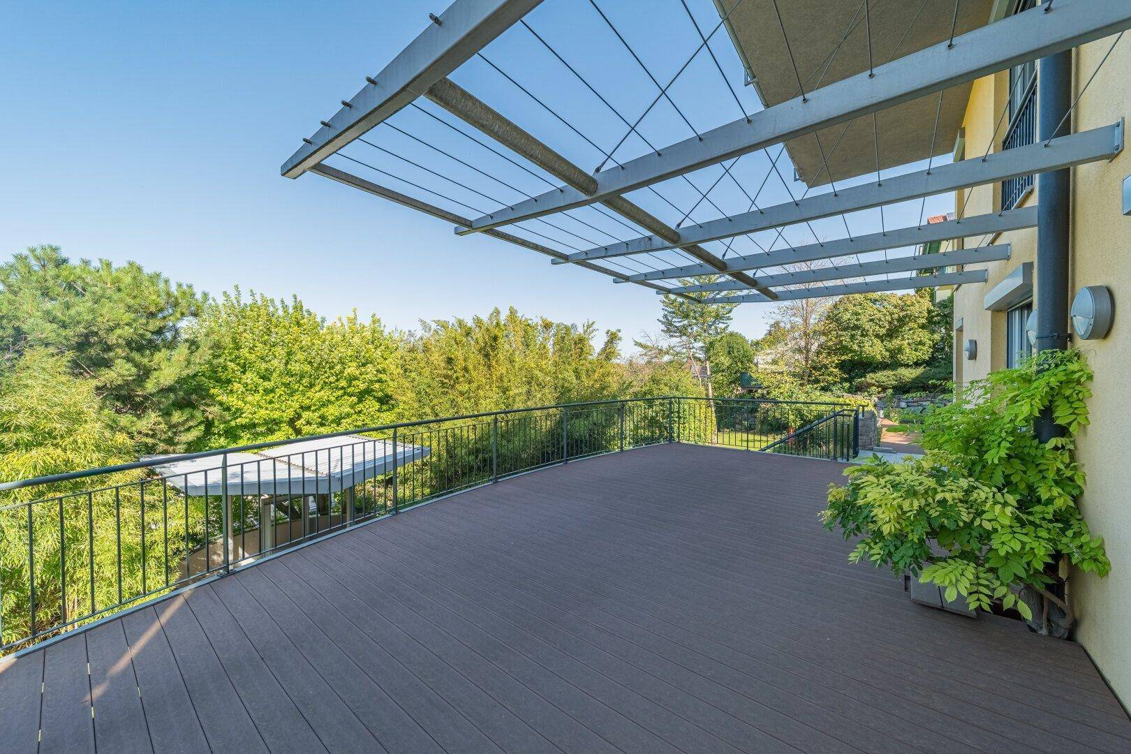 Geräumige Holzterrasse mit Pergola und weitem Blick auf die umliegende grüne Landschaft und Bäume.
