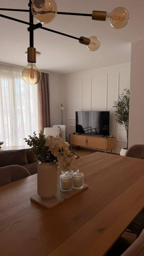 Essbereich mit Holztisch und moderner Beleuchtung, im Hintergrund ist der Wohnbereich sichtbar.