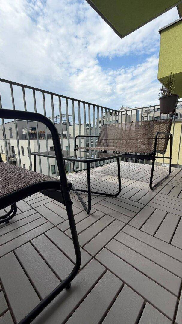 Balkon mit Holzdielen und Outdoor-Möbeln, bietet einen Blick auf die umliegenden Gebäude.