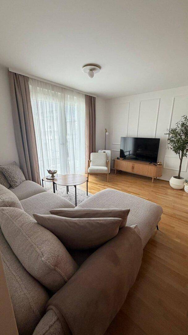 Gemütliches Wohnzimmer mit großem Sofa, Fernseher und dekorativer Wandverkleidung, hell durch große Fenster.