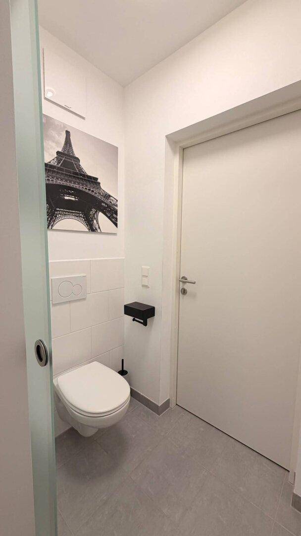 Modernes Gäste-WC mit wandhängender Toilette und grauen Fliesen, dekoriert mit einem Bild.