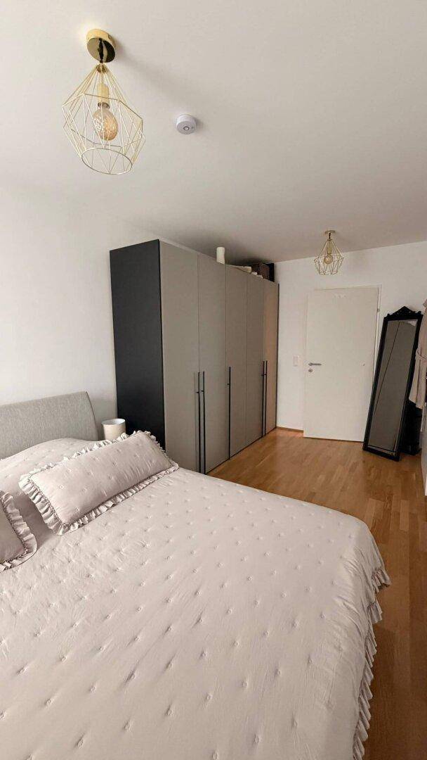 Schlafzimmer mit Doppelbett, großem Kleiderschrank und Holzboden, beleuchtet von modernen Pendelleuchten.