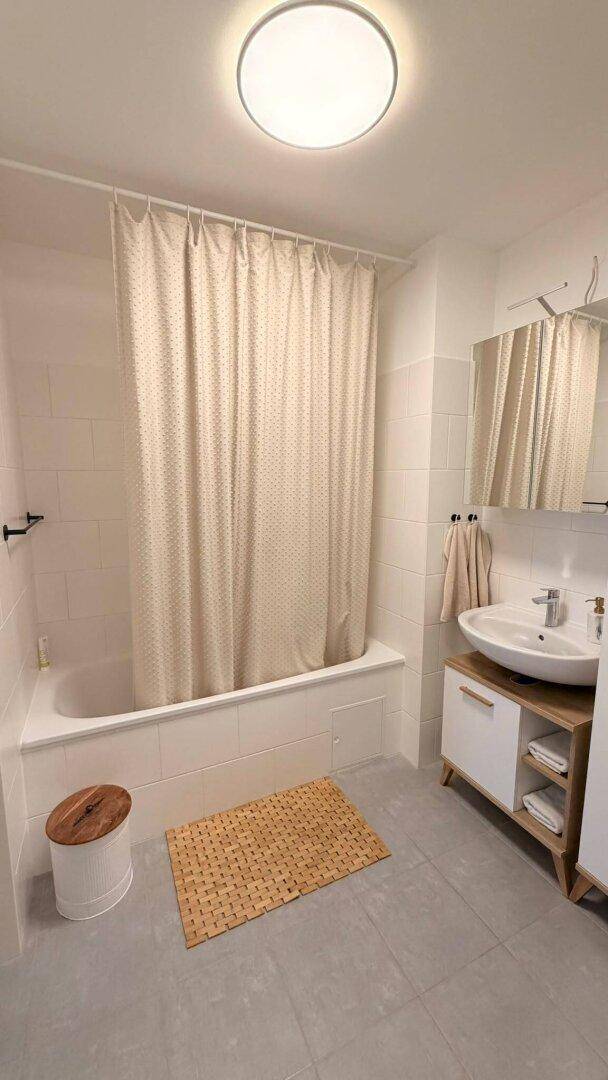 Badezimmer mit Badewanne, Duschvorhang und Einzelwaschbecken, auf grauen Fliesen.