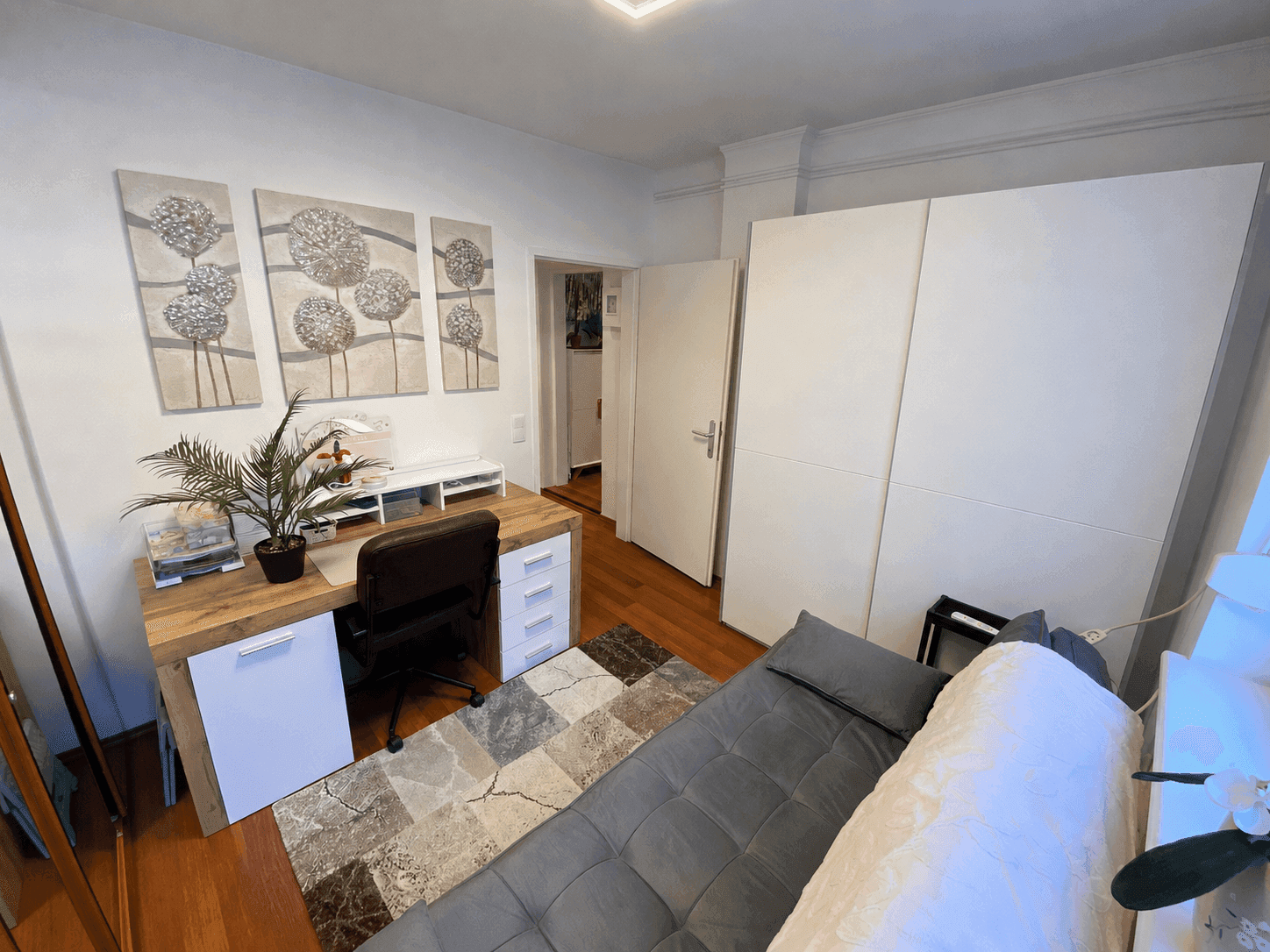 Funktionales Arbeitszimmer mit Schreibtisch, Tagesbett und Kleiderschrank auf Holzboden.