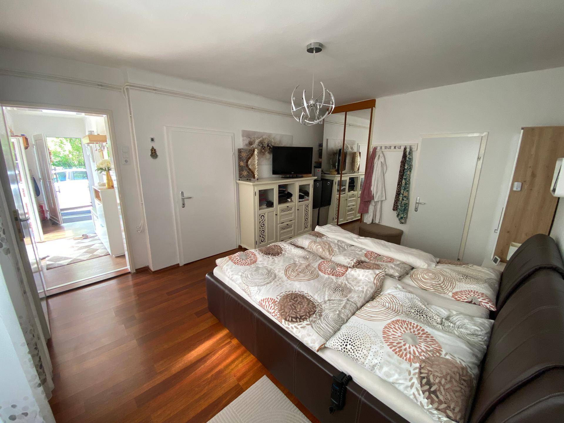 Gemütliches Schlafzimmer mit Doppelbett, Fernseher und Kleiderschrank auf Holzboden.