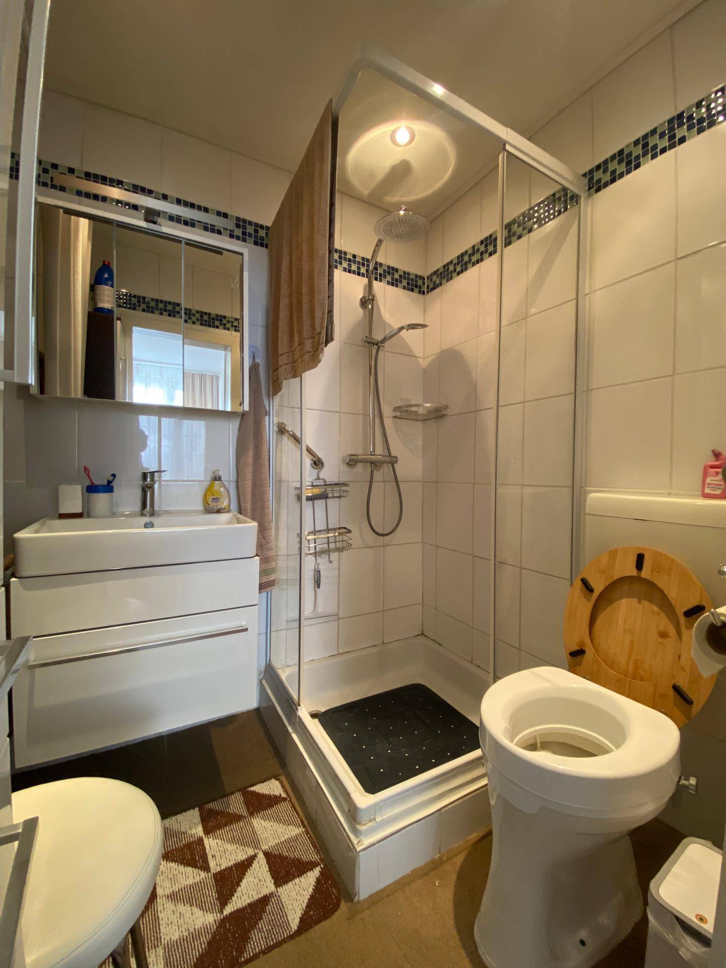 Badezimmer mit Duschkabine, Toilette und Waschbecken, gefliest in Weiß und Blau.
