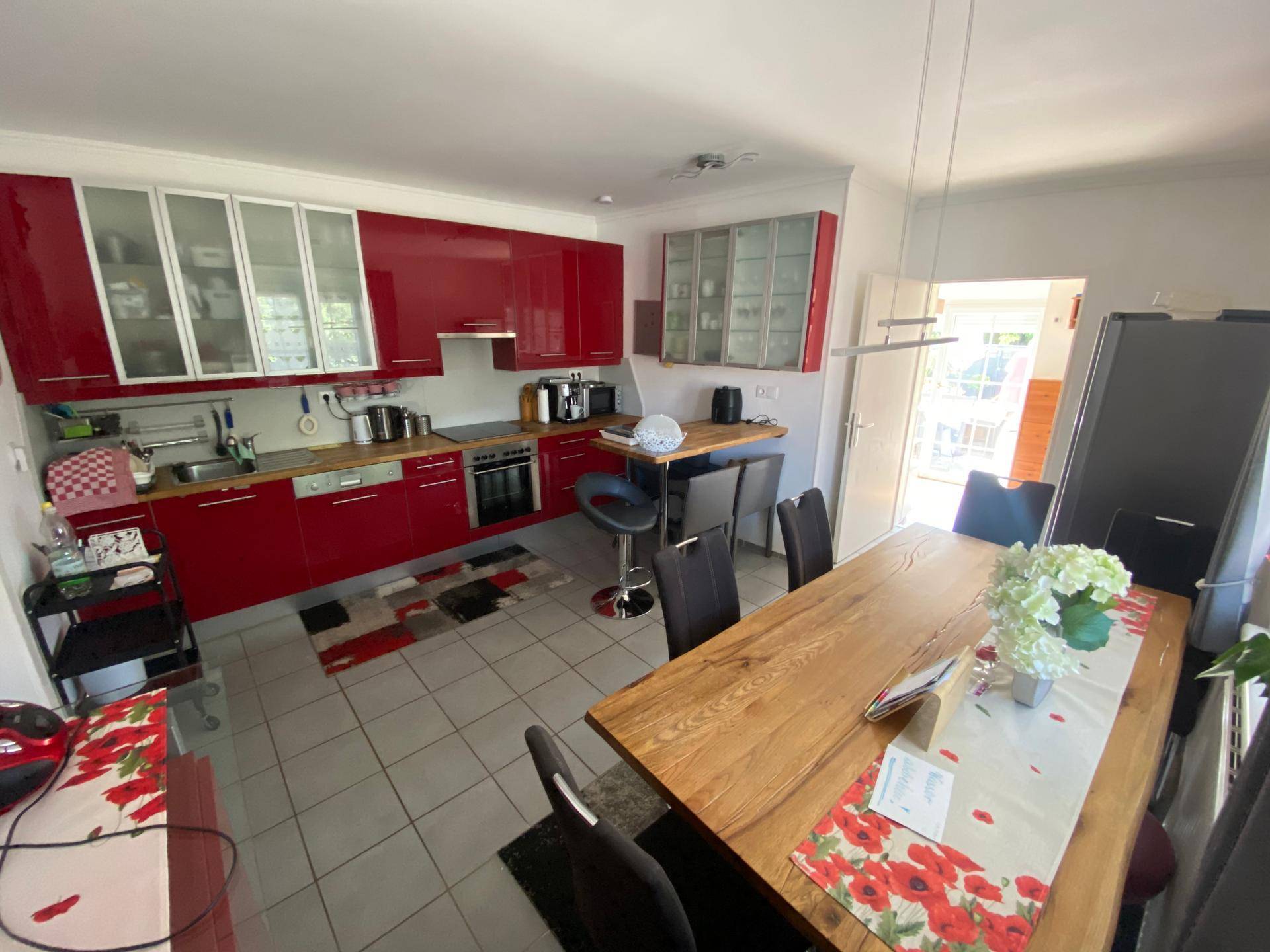 Moderne Küche mit roten Schränken, Esstisch und integrierter Frühstücksbar.