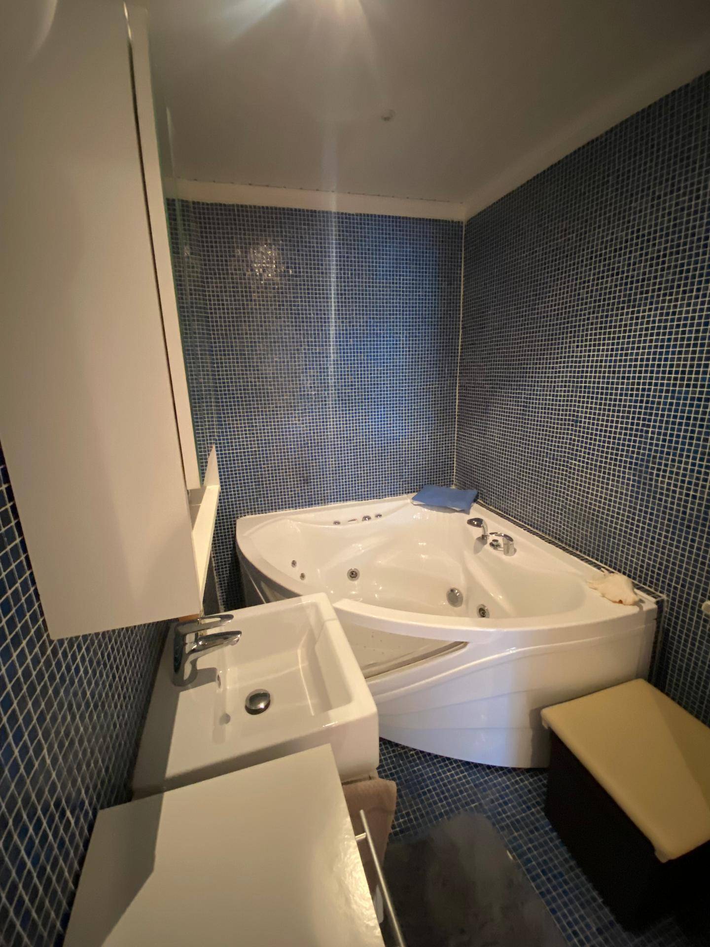 Badezimmer mit blauen Mosaikfliesen, Eck-Whirlpool und modernem Waschbecken.