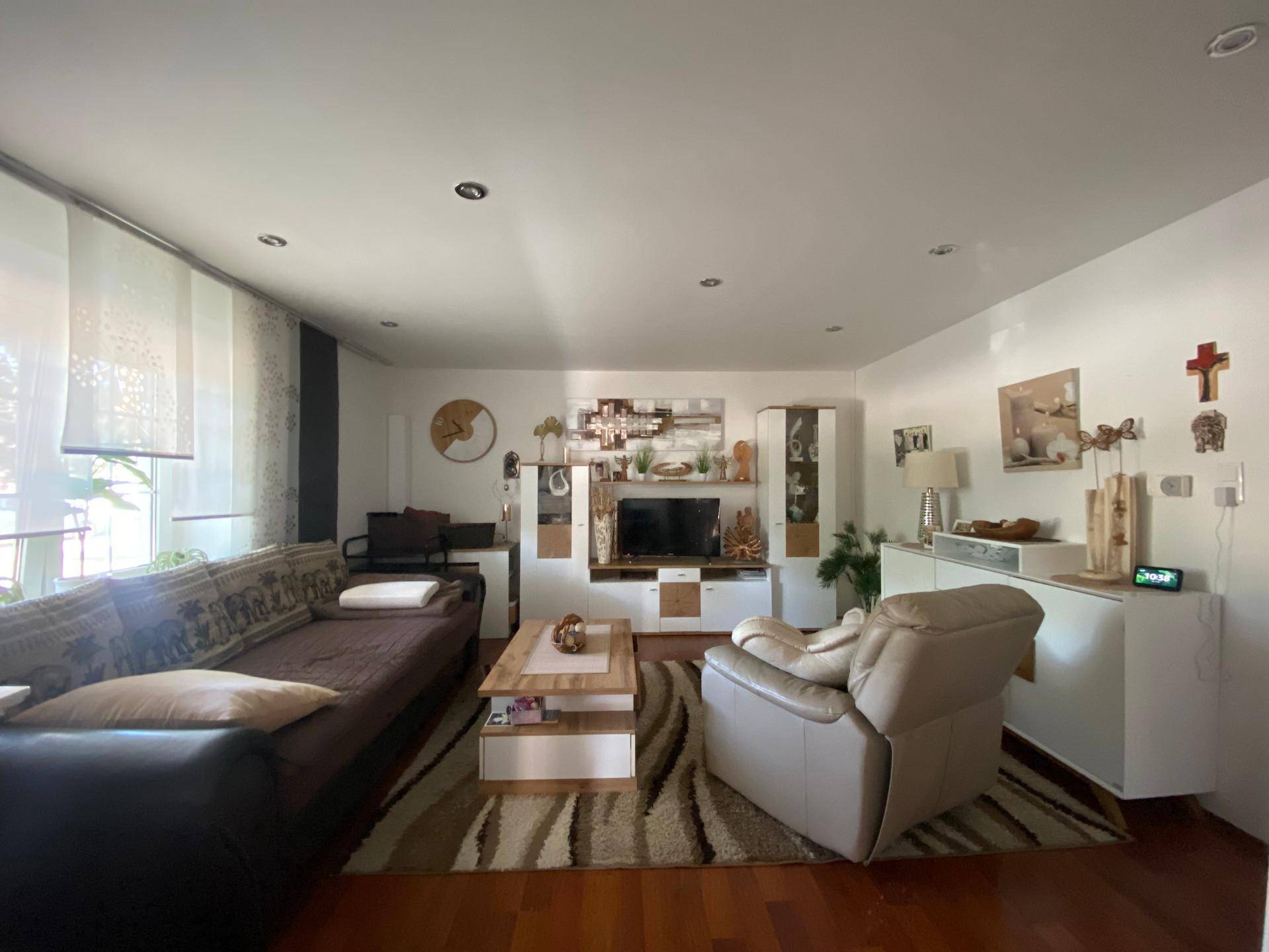 Gemütliches Wohnzimmer mit Sofa, Sessel, Couchtisch und Unterhaltungsmöbeln auf Holzfußboden.