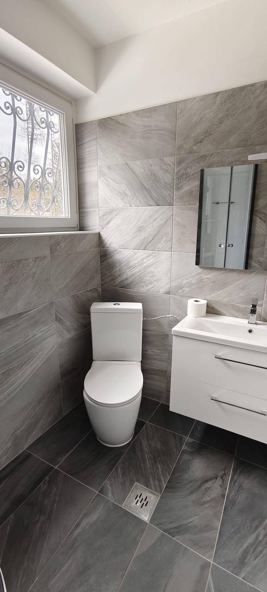 Zeitgemäßes Badezimmer mit WC, Waschtisch und großformatigen grauen Wand- und Bodenfliesen.