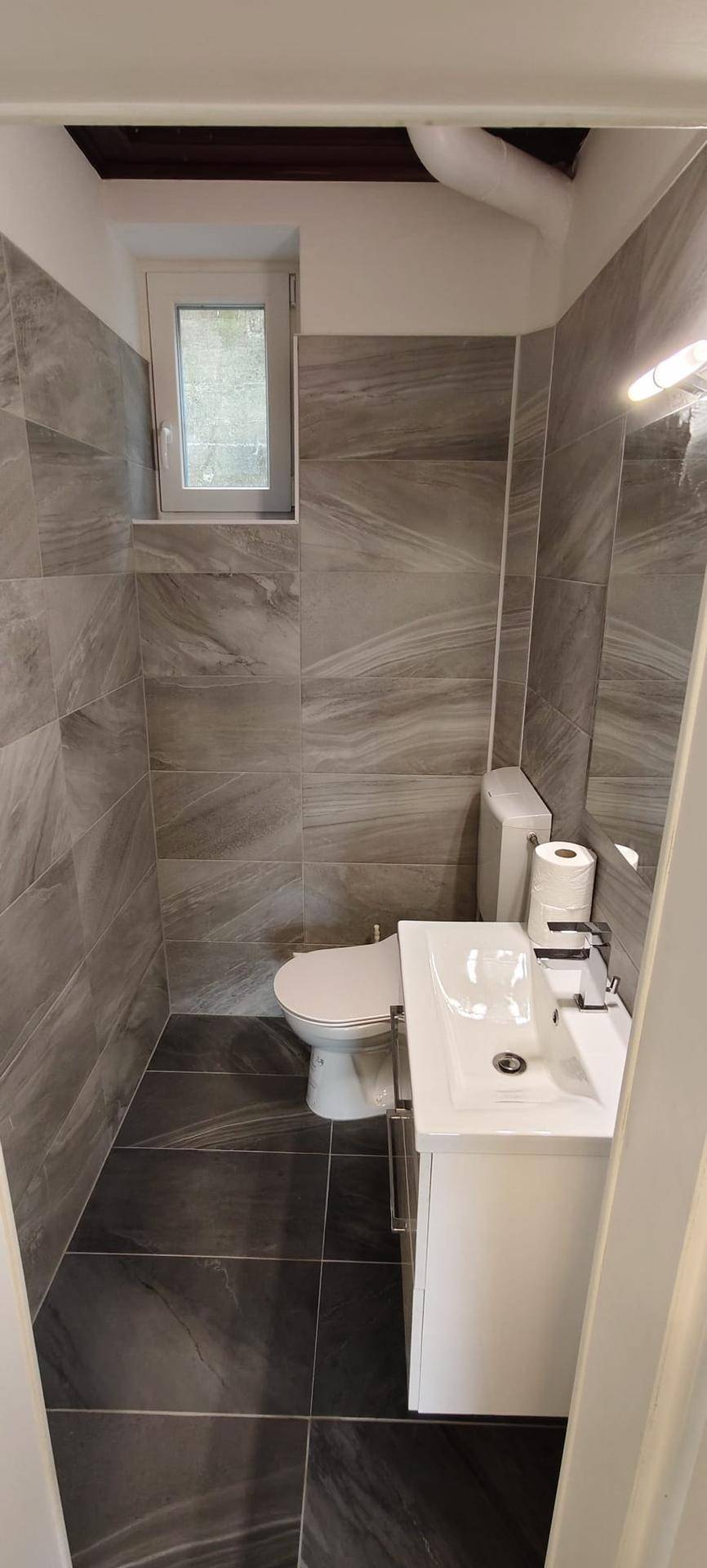 Kleines Badezimmer mit WC, Waschtisch und modernen grauen Fliesen.