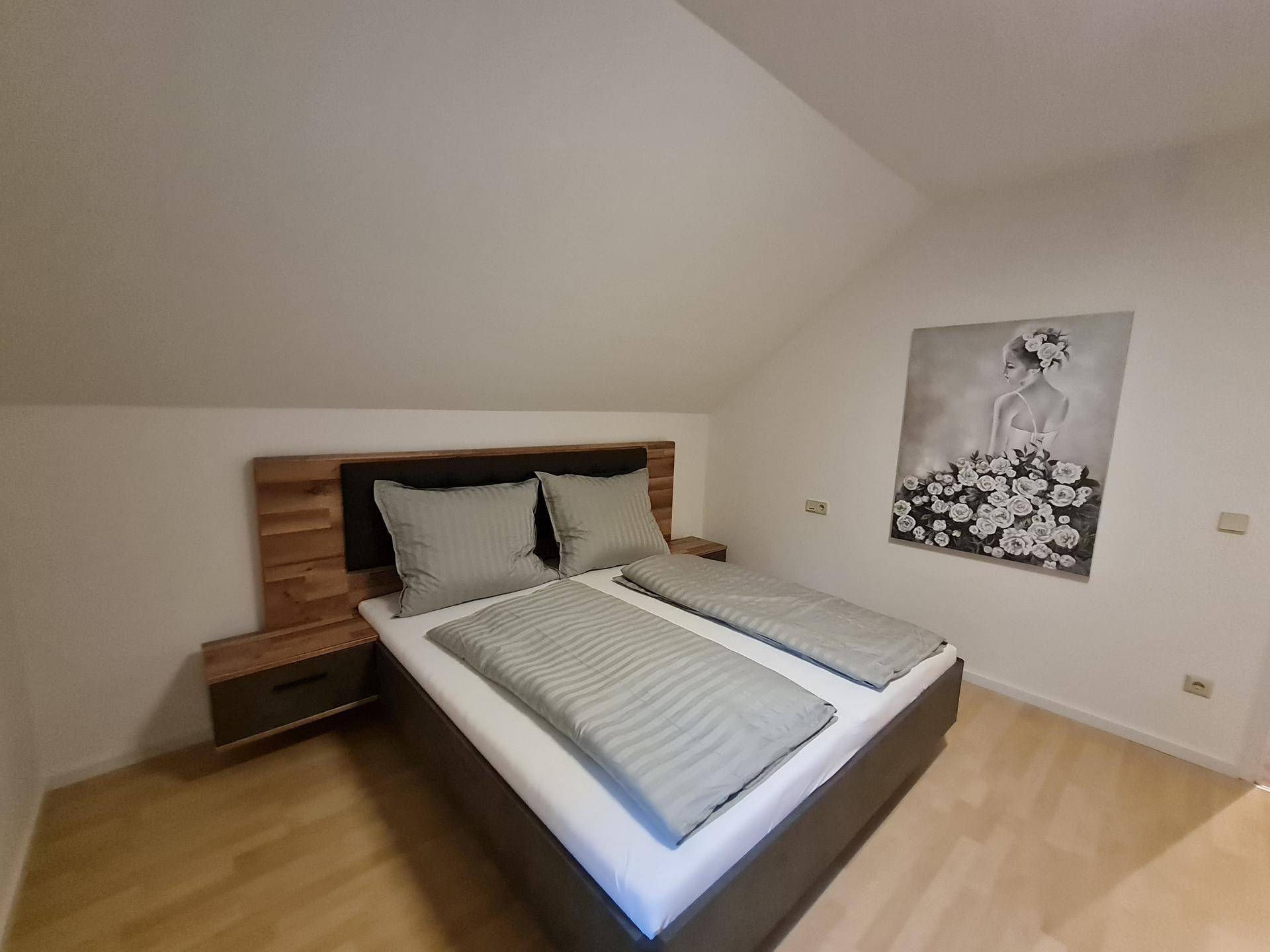 Helles Schlafzimmer im Dachgeschoss mit Doppelbett, Holzkopfteil und Kunst an der Wand.