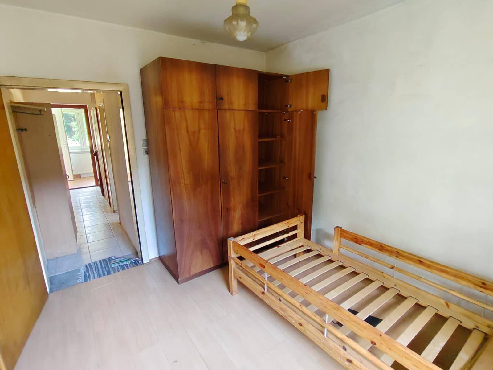 Schlafzimmer mit großem Holzschrank und Blick auf den angrenzenden Flur mit Fliesenboden.