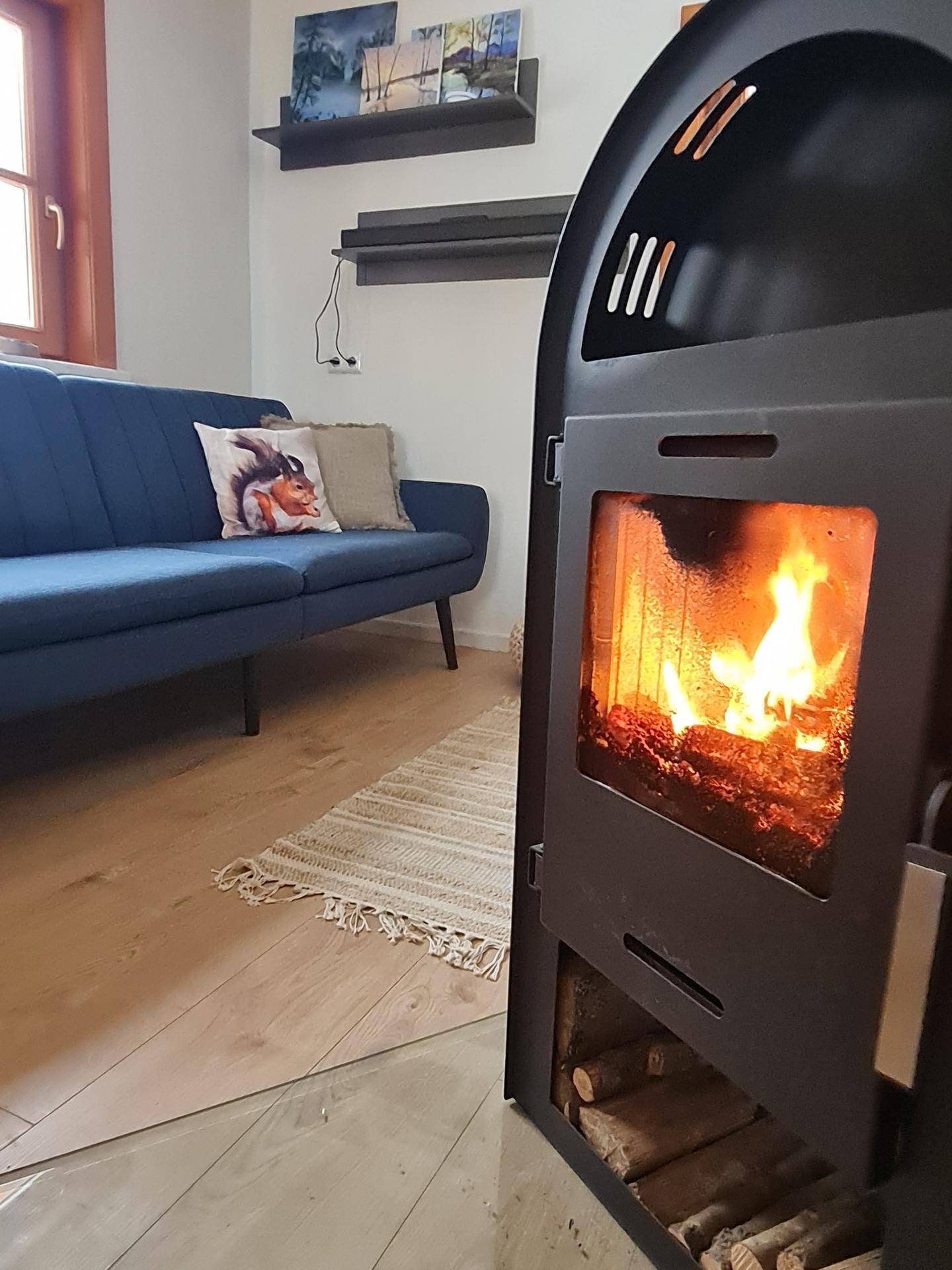 Gemütliches Wohnzimmer mit dunkelblauem Sofa, Holzboden und modernem Holzofen mit sichtbarem Feuer.