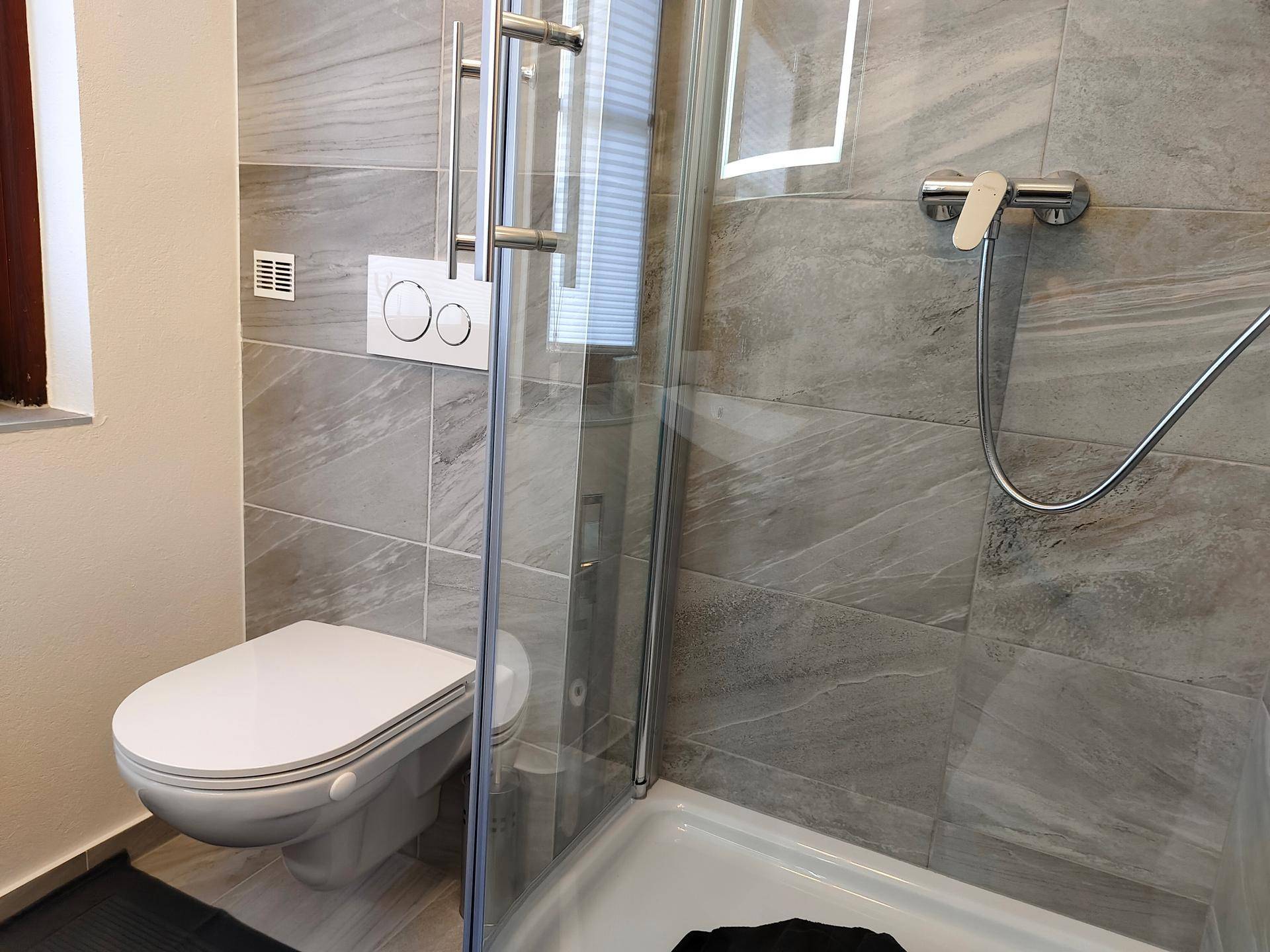 Detaillierte Ansicht der modernen Duschkabine und des wandhängenden WCs im Badezimmer.