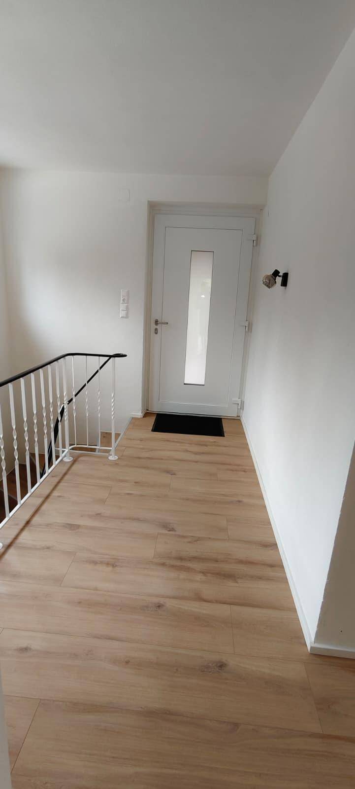 Eingangsbereich mit heller Tür, modernem Laminatboden und Treppengeländer.