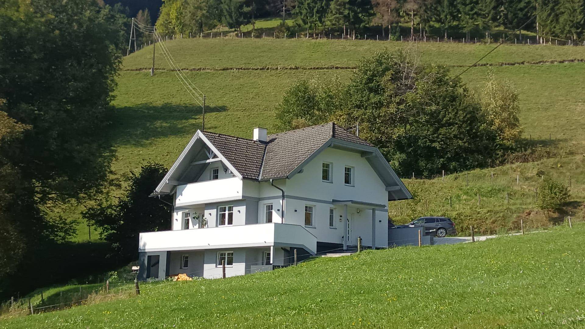 Freistehendes Haus in Hanglage mit Balkon und Blick auf die umliegende grüne Landschaft.