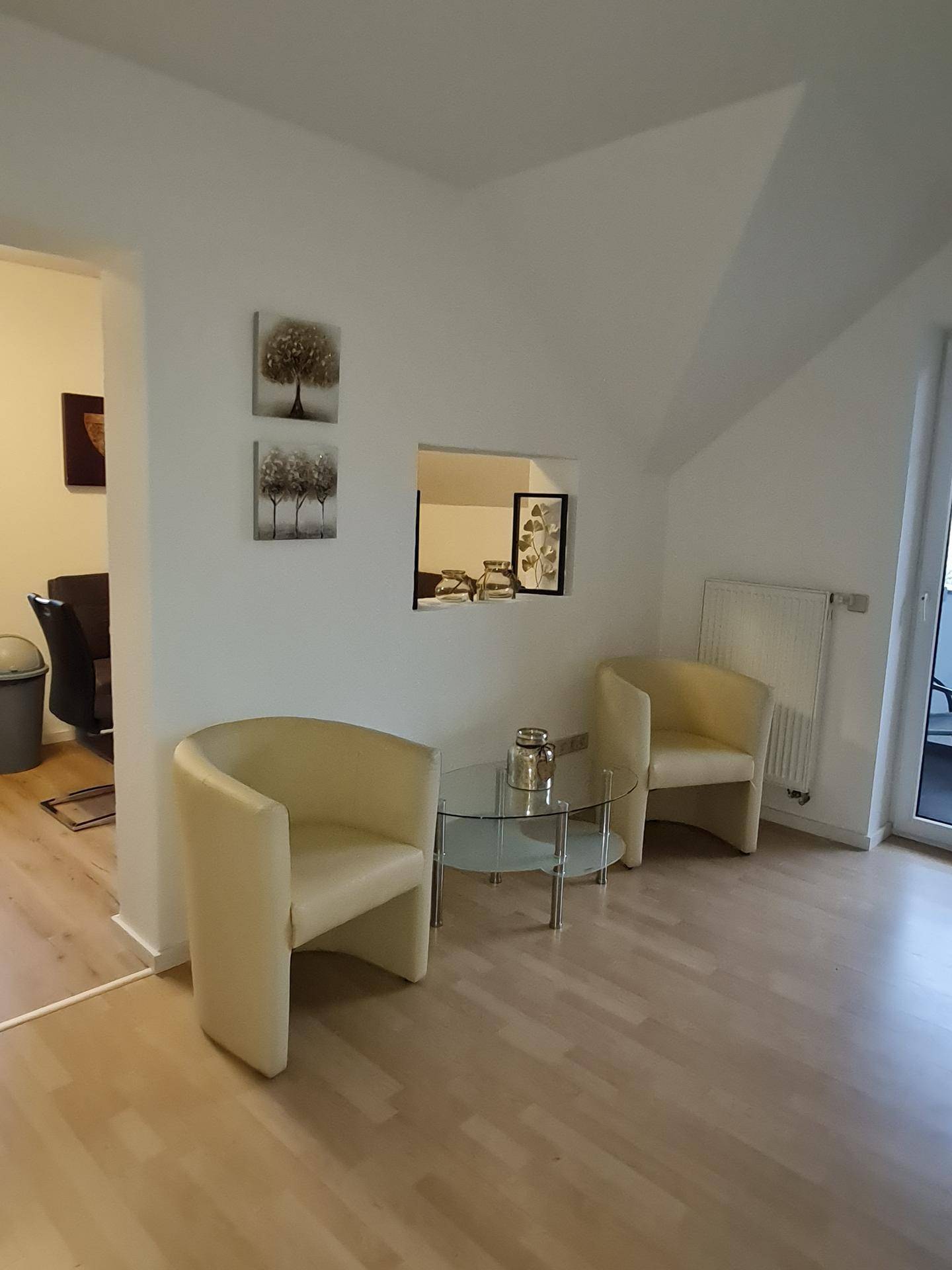 Gemütliche Sitzecke mit zwei beigen Sesseln, Glastisch und Zugang zum Außenbereich.
