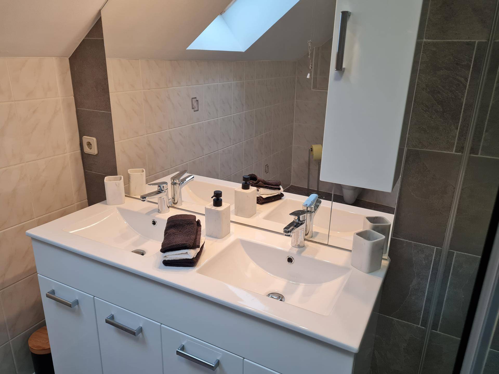 Detailansicht des Doppelwaschbeckens mit modernen Armaturen und Pflegeprodukten im Badezimmer.