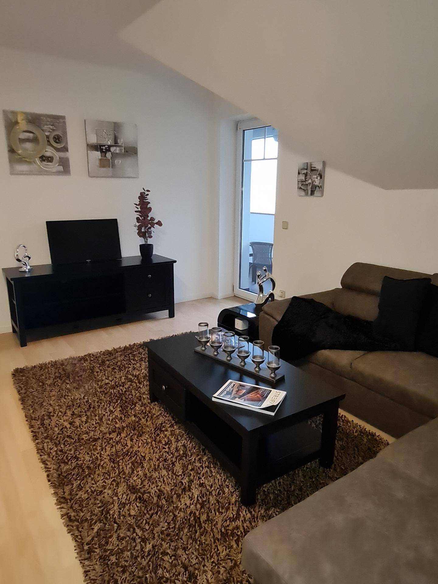Wohnzimmer mit Ecksofa, Fernsehmöbel und Zugang zu einem Balkon oder einer Terrasse.