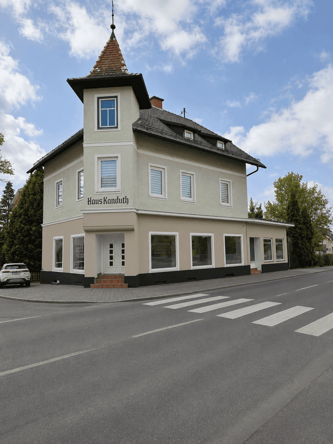 Das historische Gebäude "Haus Kanduth" an einer Straßenecke mit klarem Himmel und umliegender Vegetation.