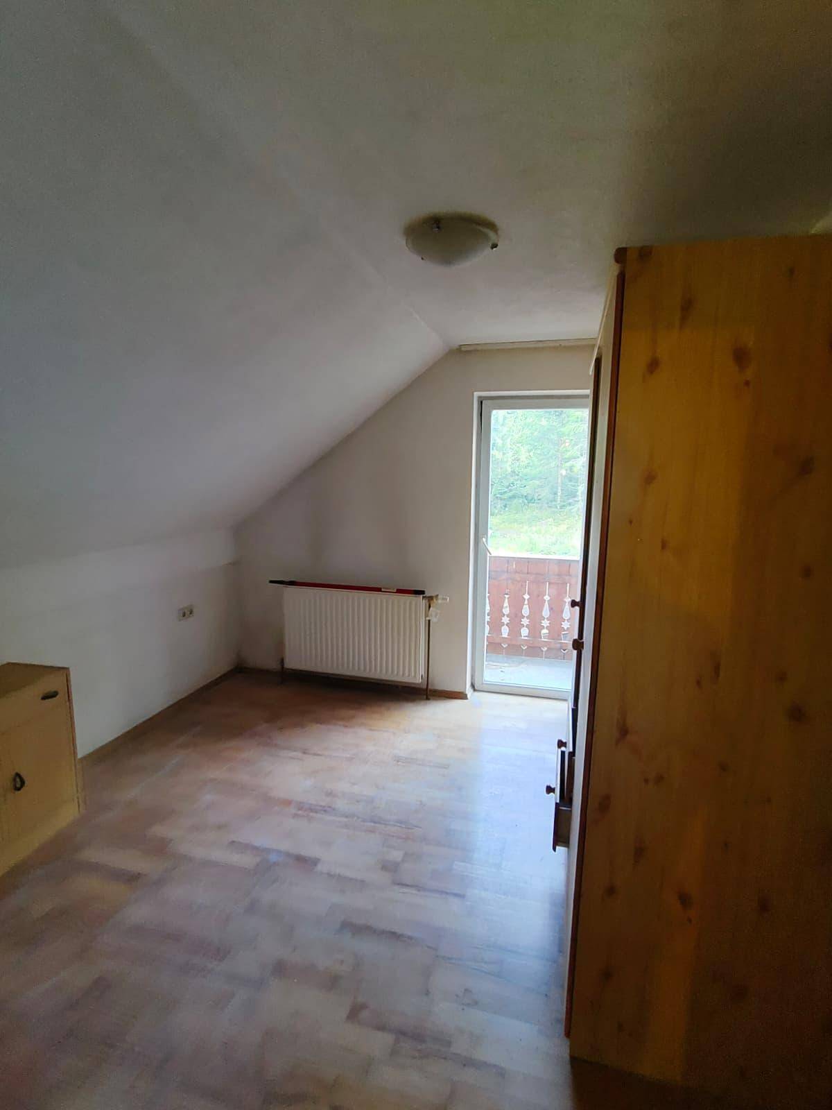 Leeres Dachzimmer mit Kleiderschrank und Balkonzugang, unter schrägen Decken, bereit zur Gestaltung.