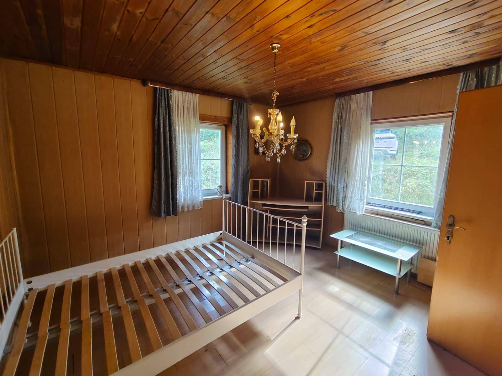 Rustikales Schlafzimmer mit Holzvertäfelung an Wänden und Decke, einem Metallbett und Kronleuchter.