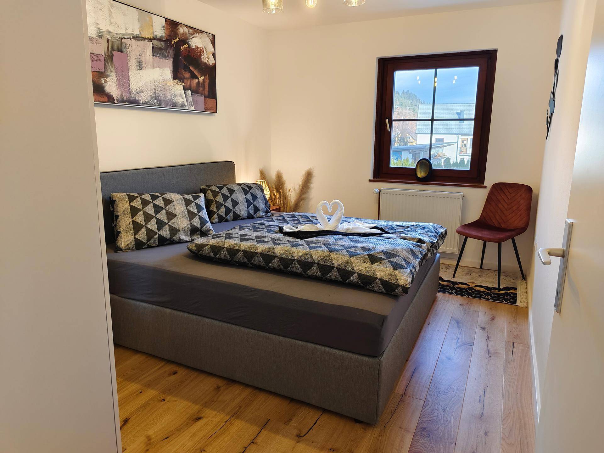 Gemütliches Schlafzimmer mit Doppelbett, Holzboden und Fenster mit Blick ins Grüne.