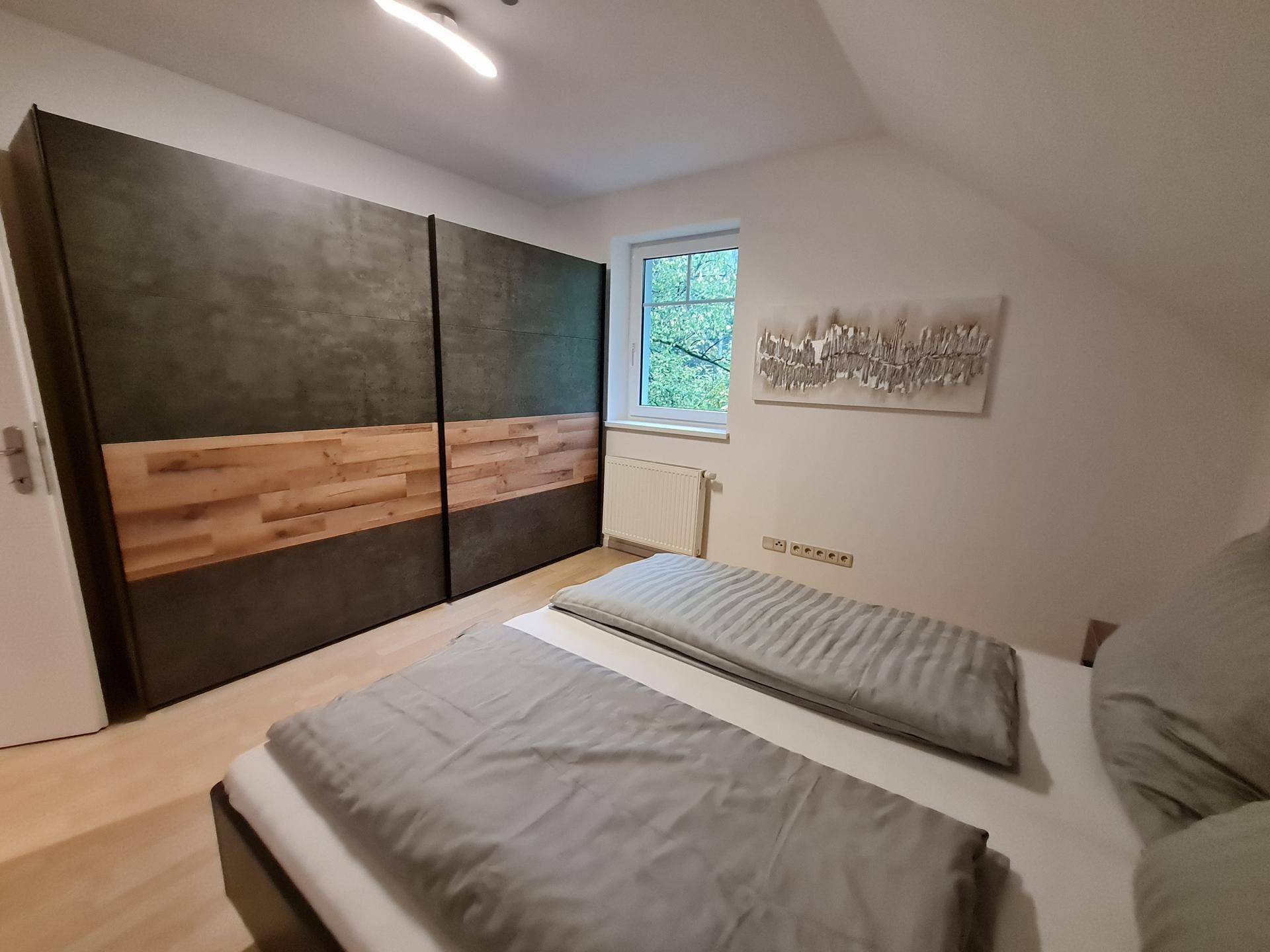 Schlafzimmer mit modernem Doppelbett, großem Kleiderschrank und Laminatboden im Dachgeschoss.