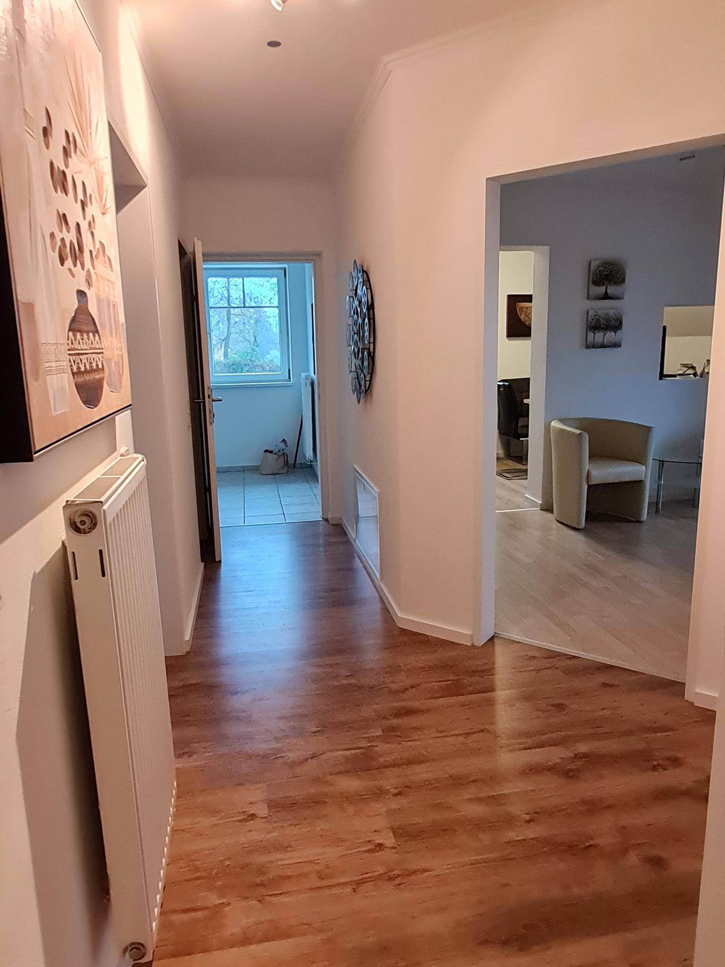 Heller Flur mit Laminatboden, Heizkörper und Durchgang zu weiteren Räumen.