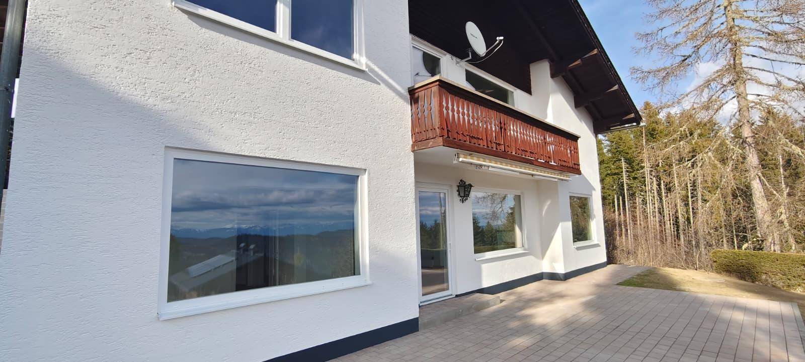 Detailansicht der Hausfassade mit Balkon, großen Fenstern und gepflasterter Terrasse.