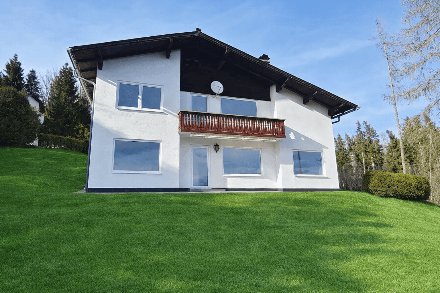Frontansicht des modernen Einfamilienhauses mit Balkon und weitläufigem Rasenbereich.