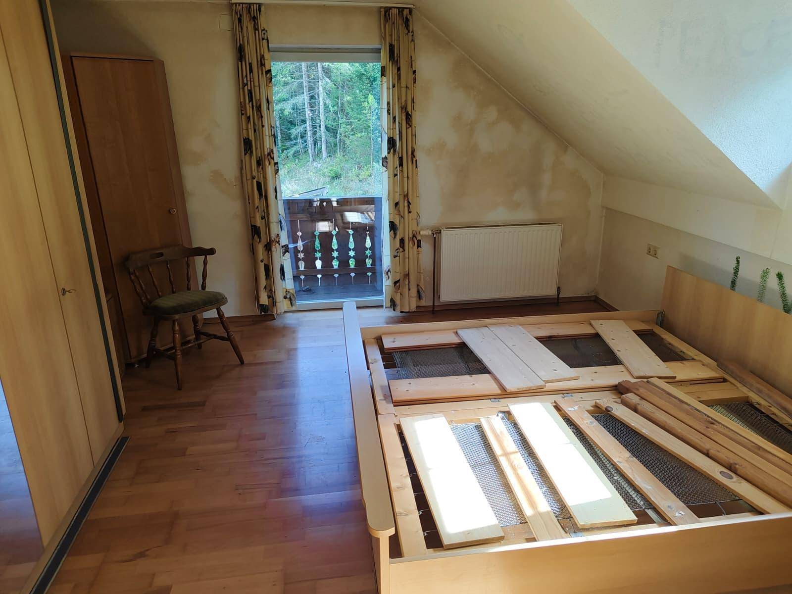 Dachschlafzimmer mit Bettgestell, Kleiderschrank und Zugang zu einem Balkon, unter schrägen Decken.