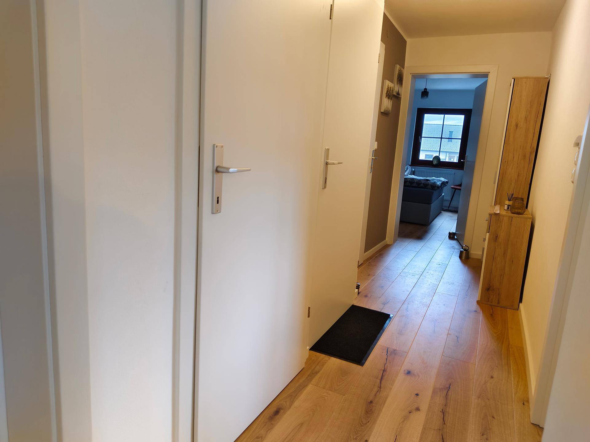 Heller Flur mit Holzboden, weißen Türen und Zugang zu weiteren Räumen.