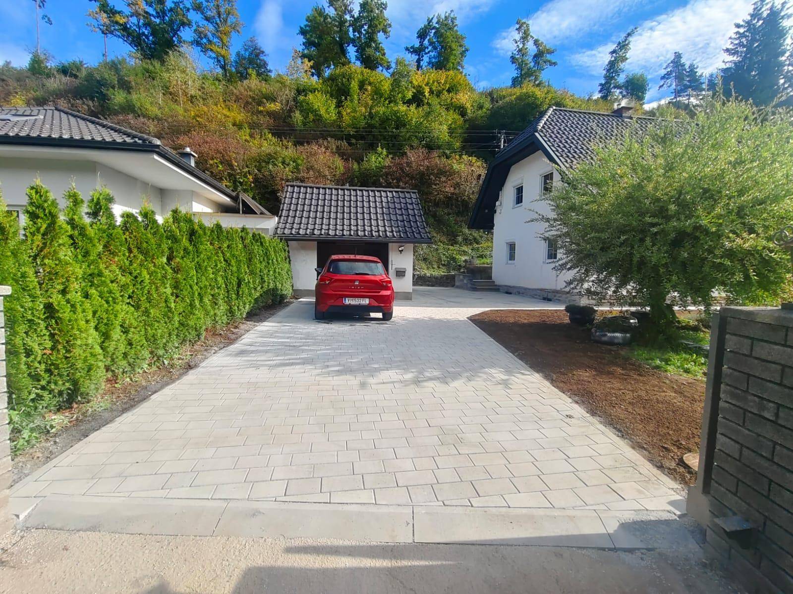 Einfamilienhaus mit gepflasterter Auffahrt, umgeben von einer grünen Hecke und Bäumen.