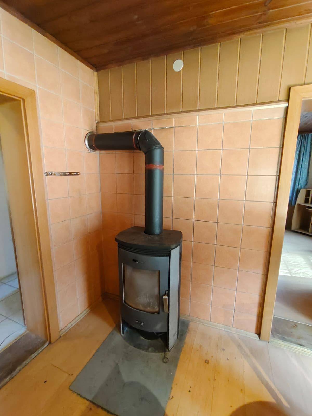 Raum mit einem Holzofen, gefliesten Wänden und einer Holzdecke, der Wärme spendet.