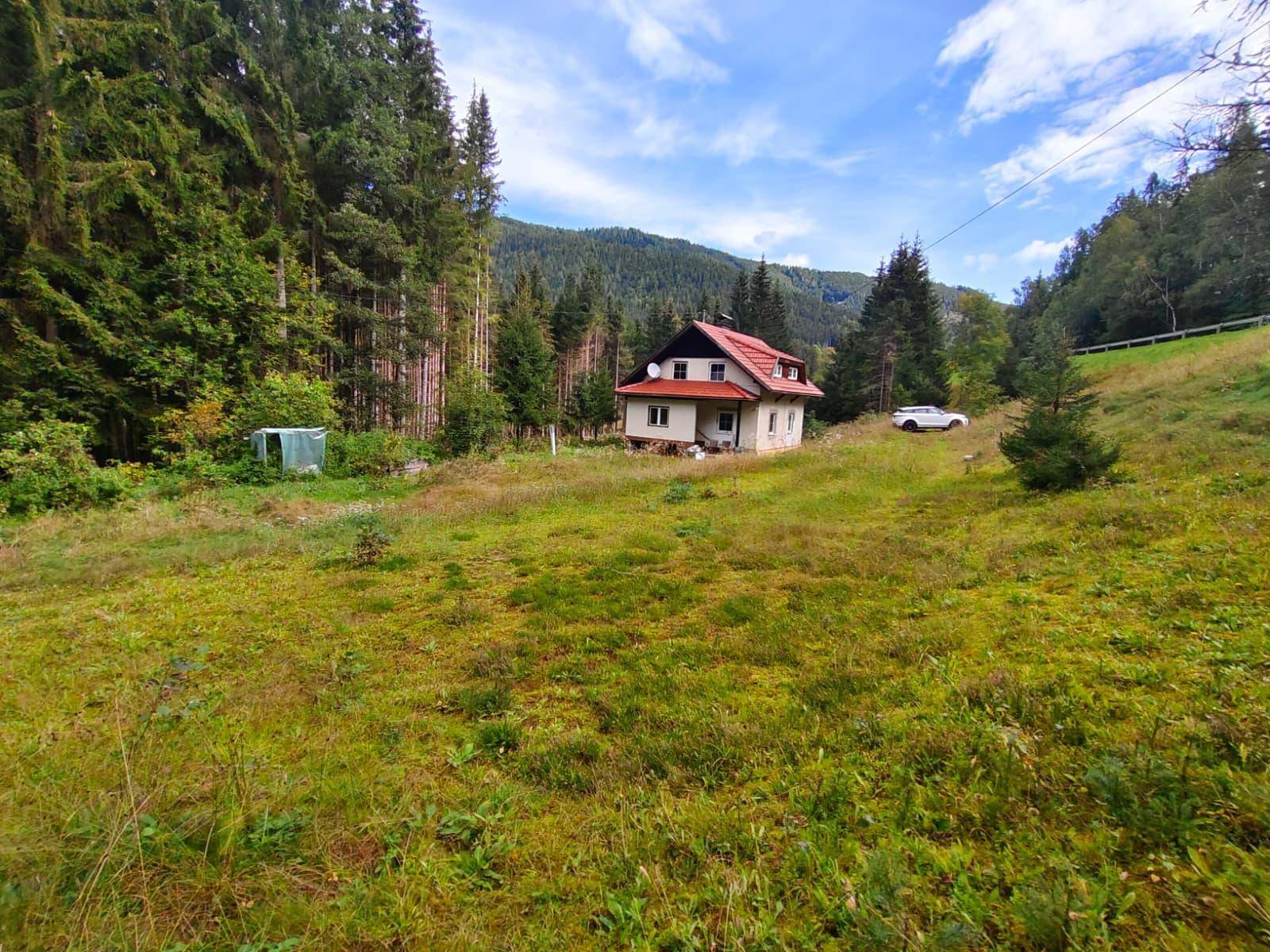Ähnliche Weitwinkelaufnahme des Hauses und seiner Umgebung, die das weite Grasfeld und den Wald zeigt.