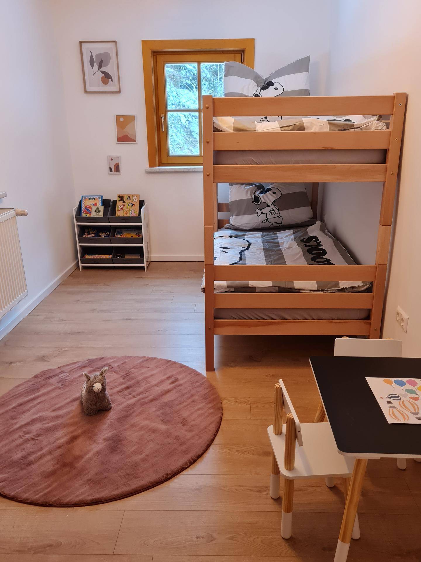 Kinderzimmer mit Etagenbett aus Holz, Holzboden, kleinem Spieltisch und Fenster.