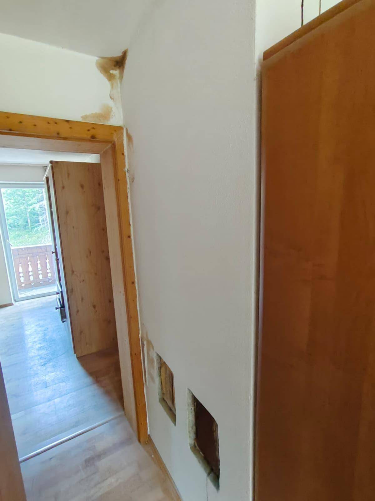 Flur mit Holztürrahmen, einer weißen Wand mit Beschädigungen und einem Holzschrank.