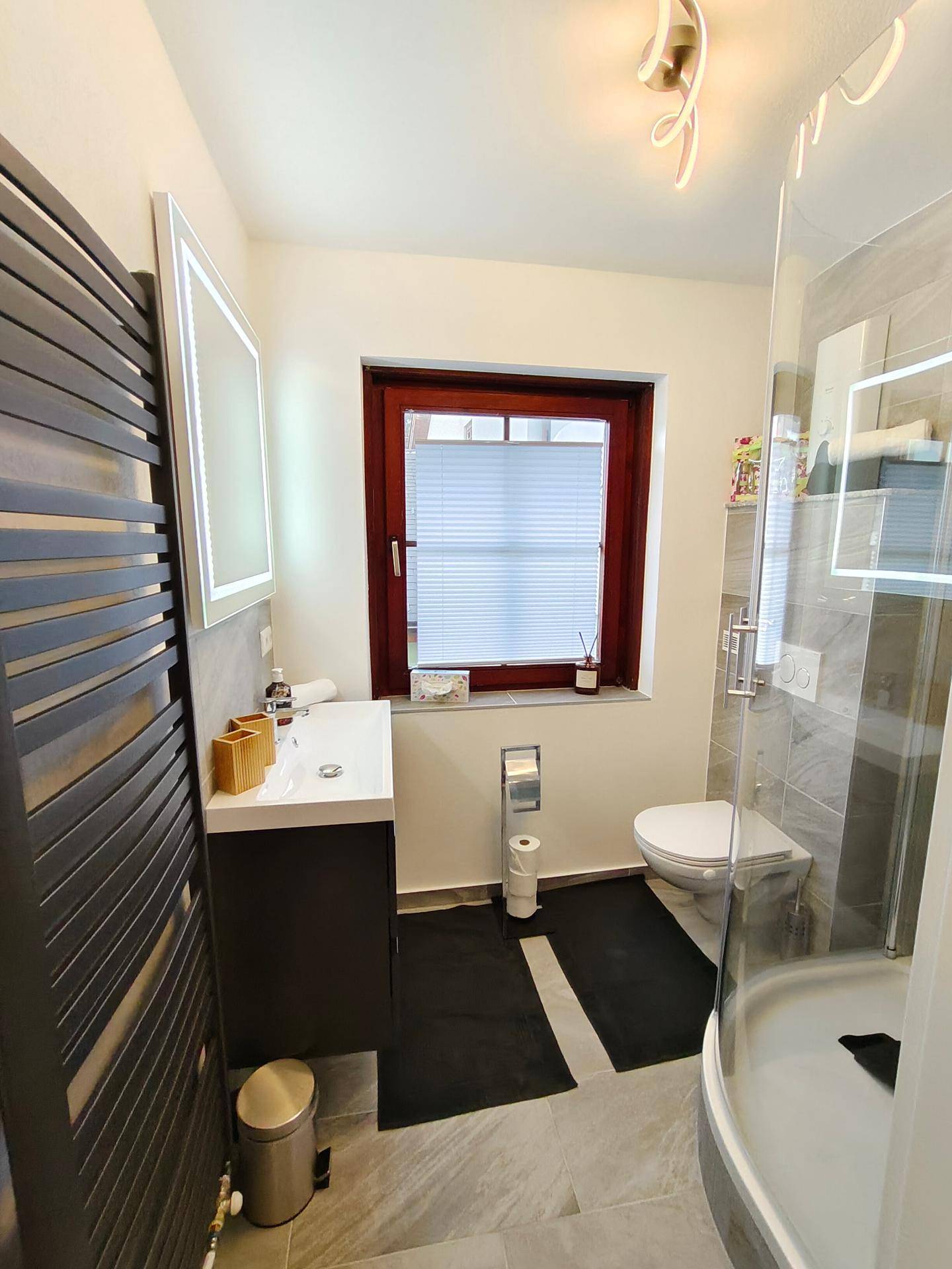 Helles Badezimmer mit Dusche, wandhängendem WC und Fenster für natürliche Belüftung.
